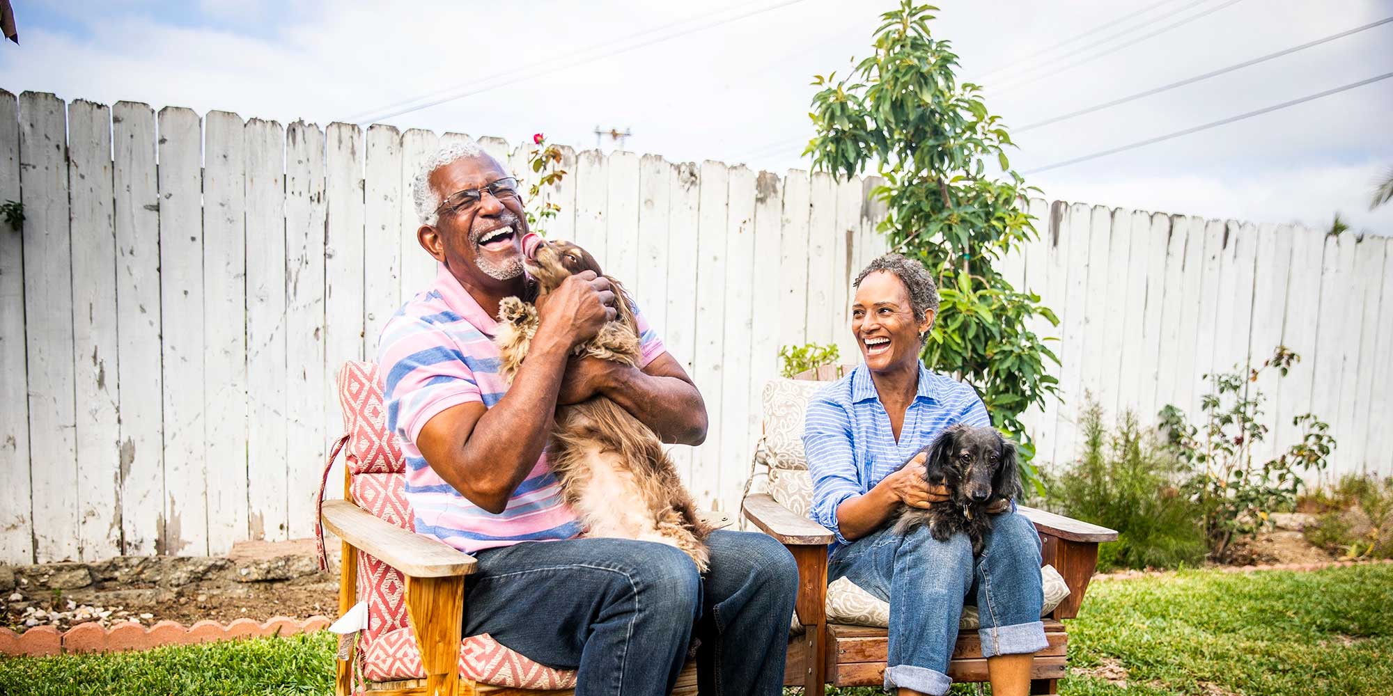 A middle-aged couple cuddle their dogs in the backyard