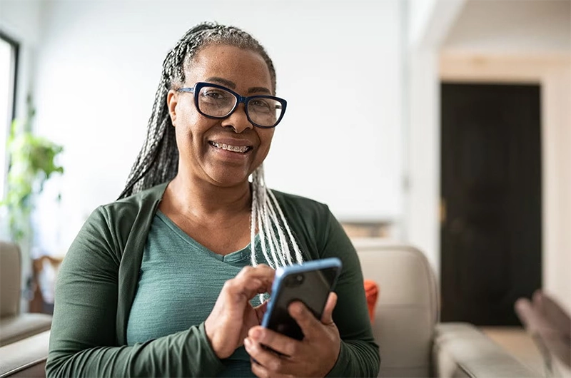A woman smiles as she taps her phone to contact someone