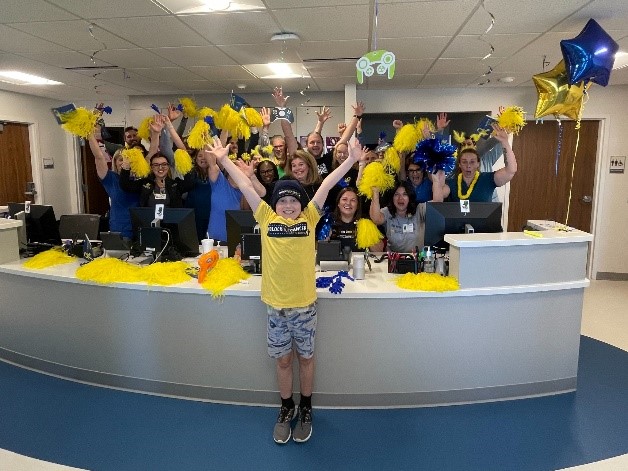 Abram's arms are raised as he proudly stands in front of staff cheering with pom-poms