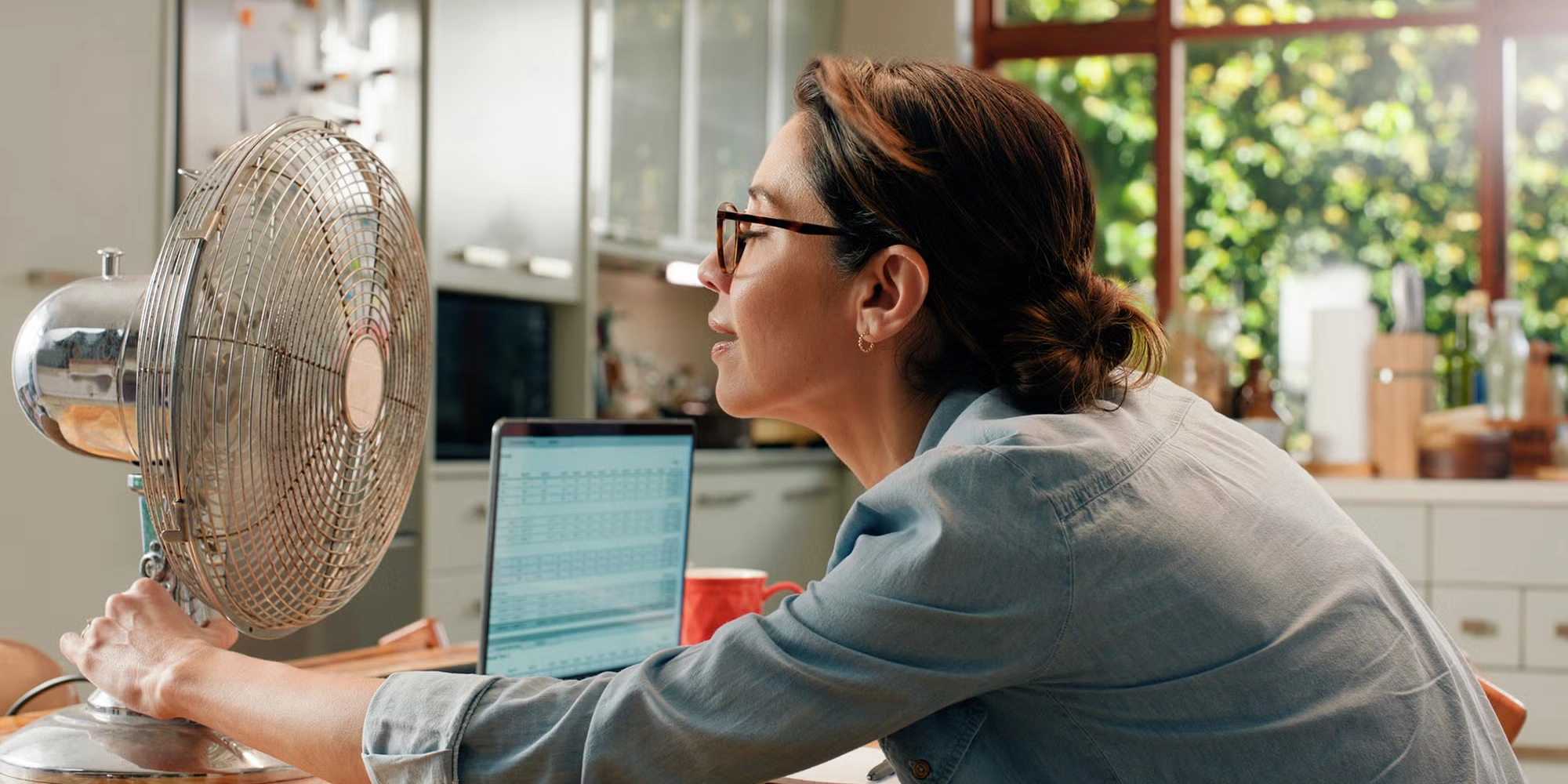 A woman experiencing a hot flash cools off using a table fan