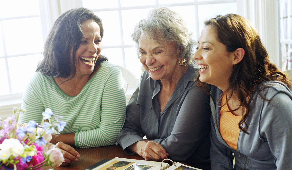 Three generations of women laughing around a table looking at a photo album.