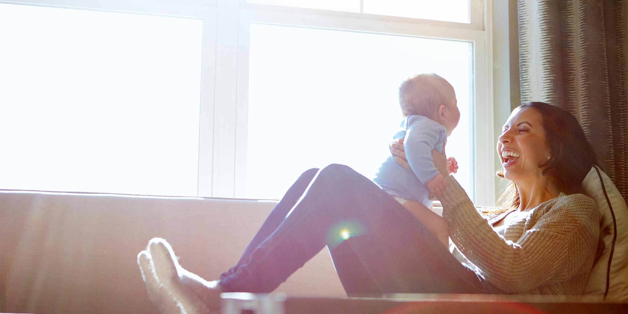 A new mother happily plays with her infant on a couch