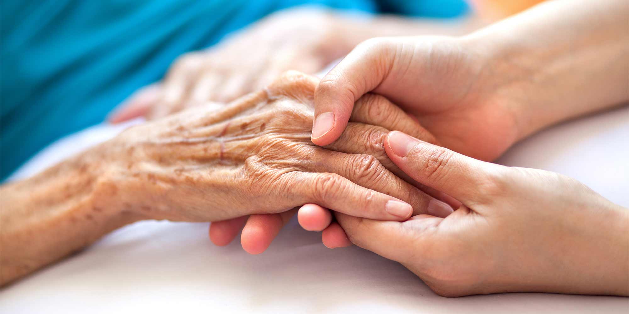 A hospice patient's hand is being held gently by a caregiver