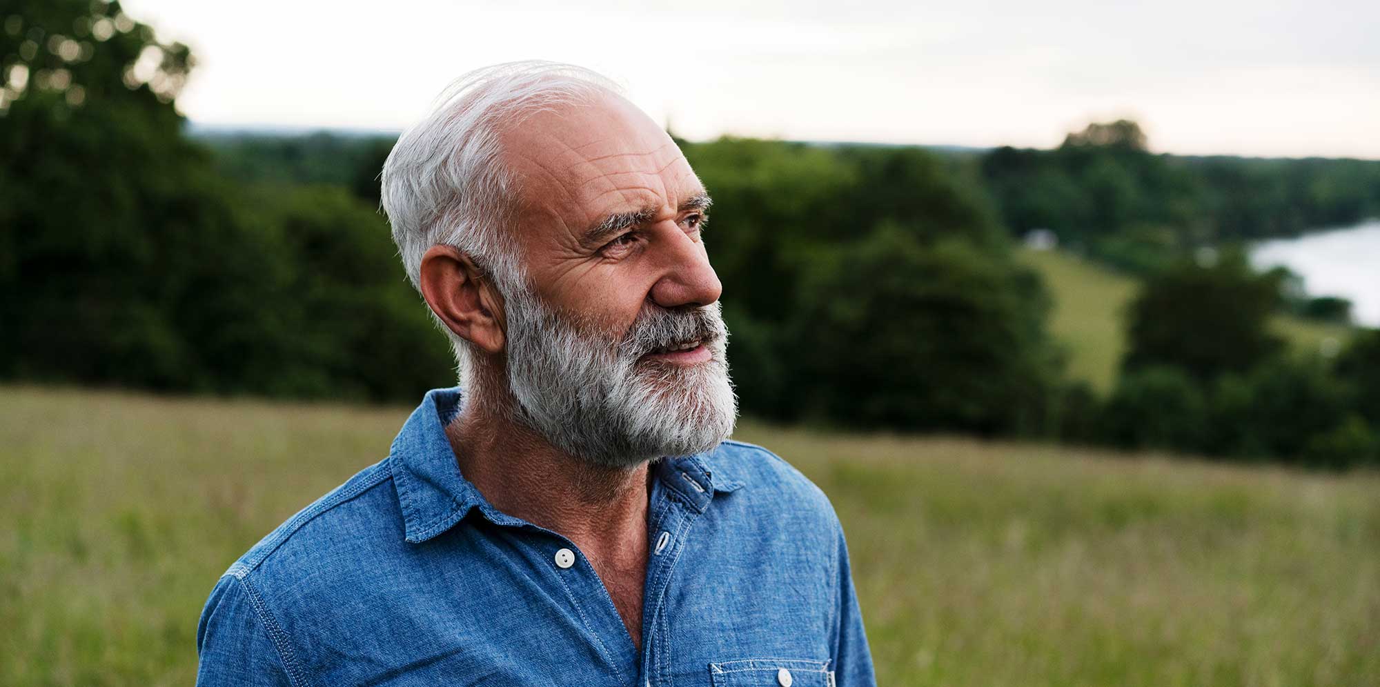 Aged man stands outside in nature and looks yonder