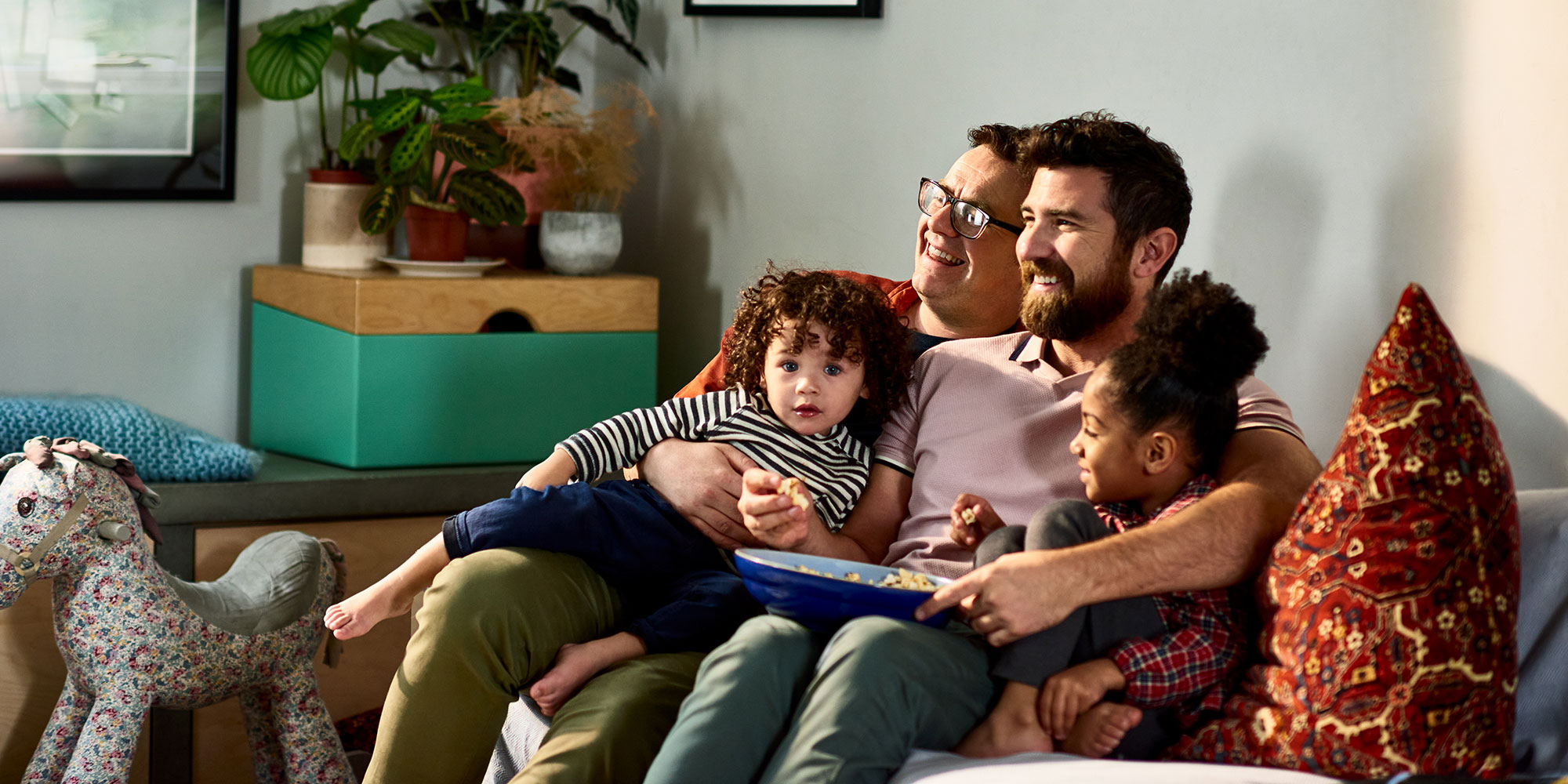Two dads snuggle and share a laugh with their children on the couch in their home