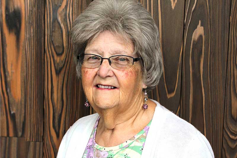 Barbara Johnson stands in front of a wooden wall wearing a white sweater