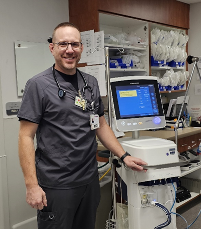 Luke in his scrubs standing next to health care equipment